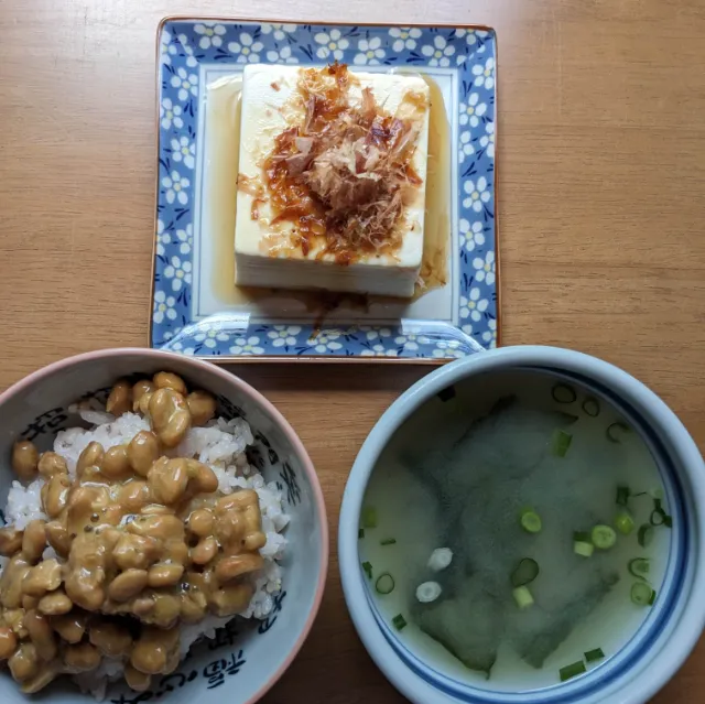 テーブルの上に納豆かけごはんの入った茶碗と即席みそ汁の入った器、冷ややっこが乗った小さなお皿を並べている様子