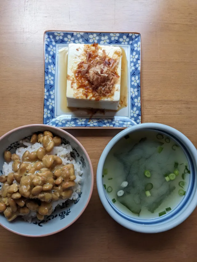 テーブルの上に納豆かけごはんの入った茶碗と即席みそ汁の入った器、冷ややっこが乗った小さなお皿を並べている様子